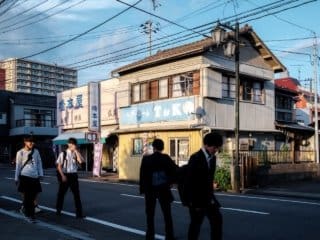 Masked Students in Traditional Japanese Neighborhood at Dusk Masked Japanese students crossing a traditional urban street at dusk.