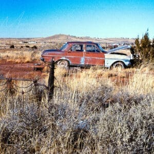 Abandoned car in desolate Arizona desert with rustic wire fence.
