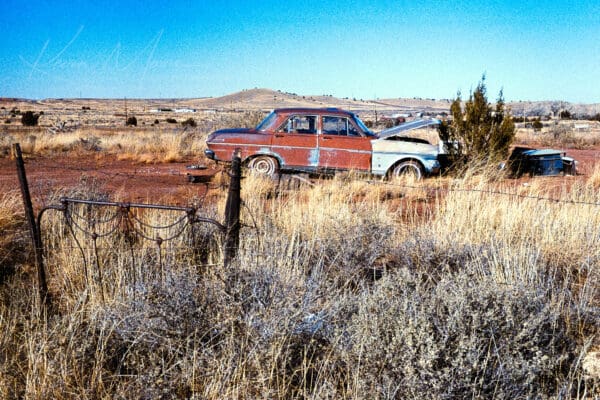 Abandoned car in desolate Arizona desert with rustic wire fence.