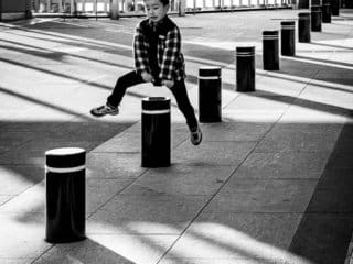 Young boy playing hopscotch among urban pillars in a cityscape.