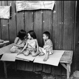 Children sharing a candid moment on rustic bench in rural Philippines, B&W photograph.