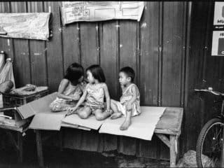 Children sharing a candid moment on rustic bench in rural Philippines, B&amp;W photograph.