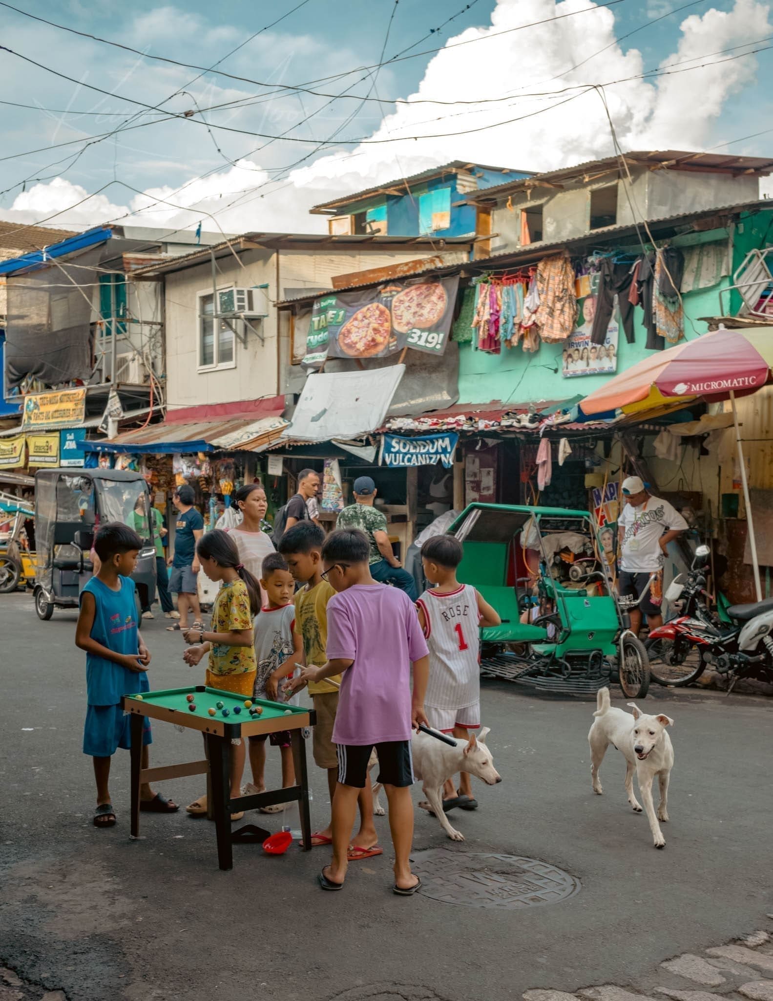 Children playing billiards on a lively street with pedestrians and motorcycles.