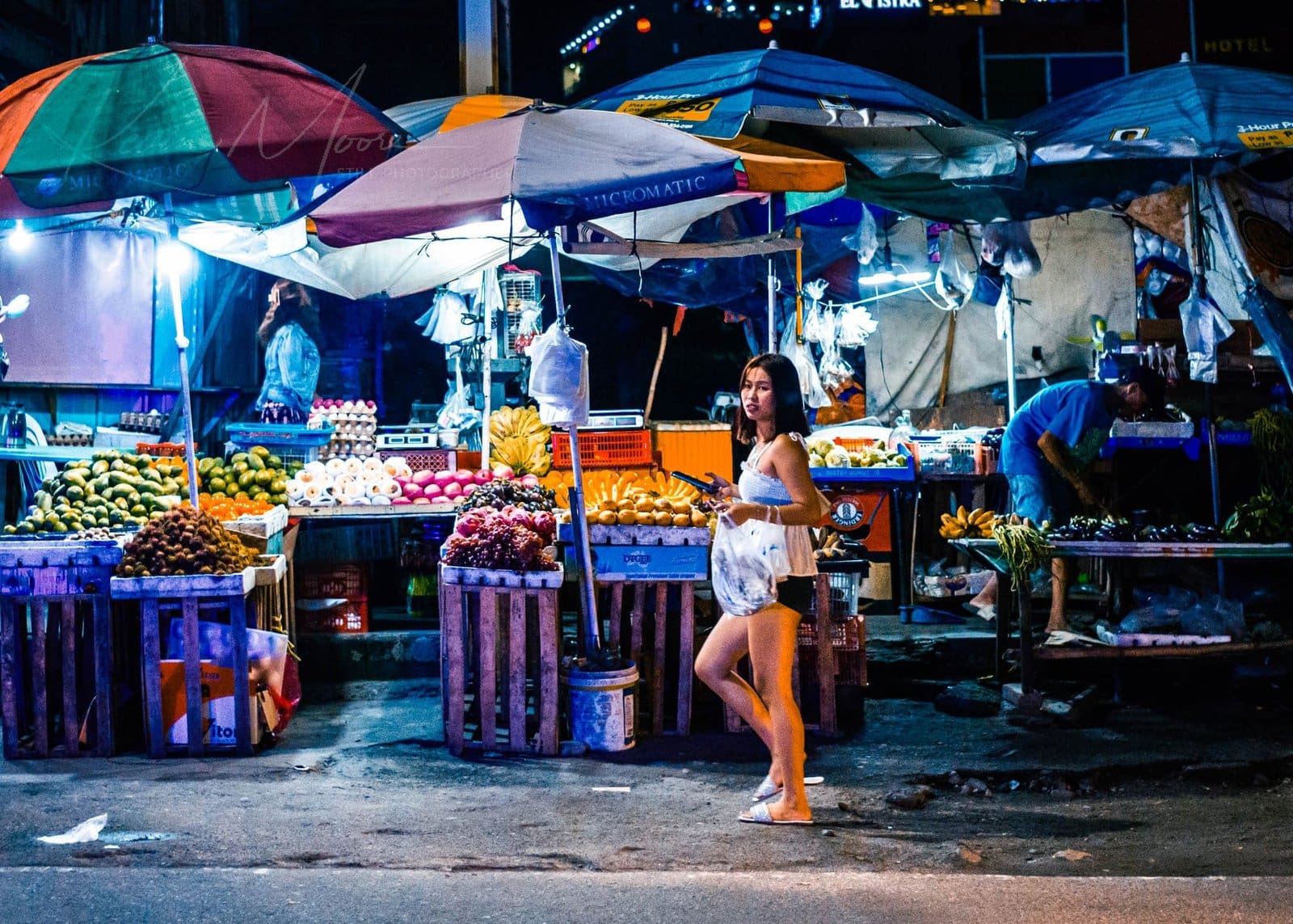 Colorful night market with vibrant fruit stalls and busy shoppers in an urban setting.