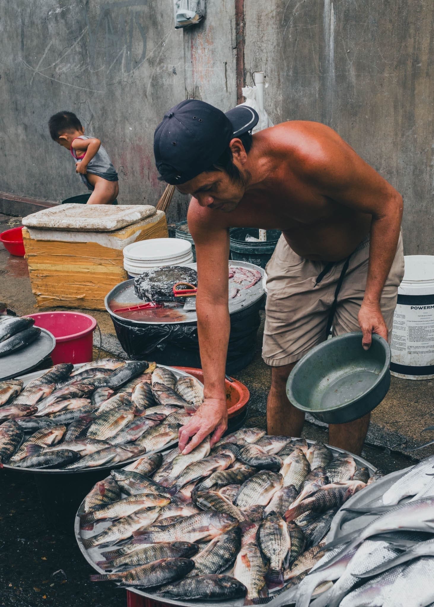 Philippines Fish market scene with vendor arranging fish and child nearby.