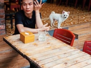 Hanoi Outdoor Cafe Young man in Hanoi cafe talking on phone with white dog at table.