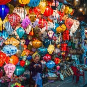 Shopkeeper amidst colorful traditional lanterns in Hoi An, Vietnam at dusk
