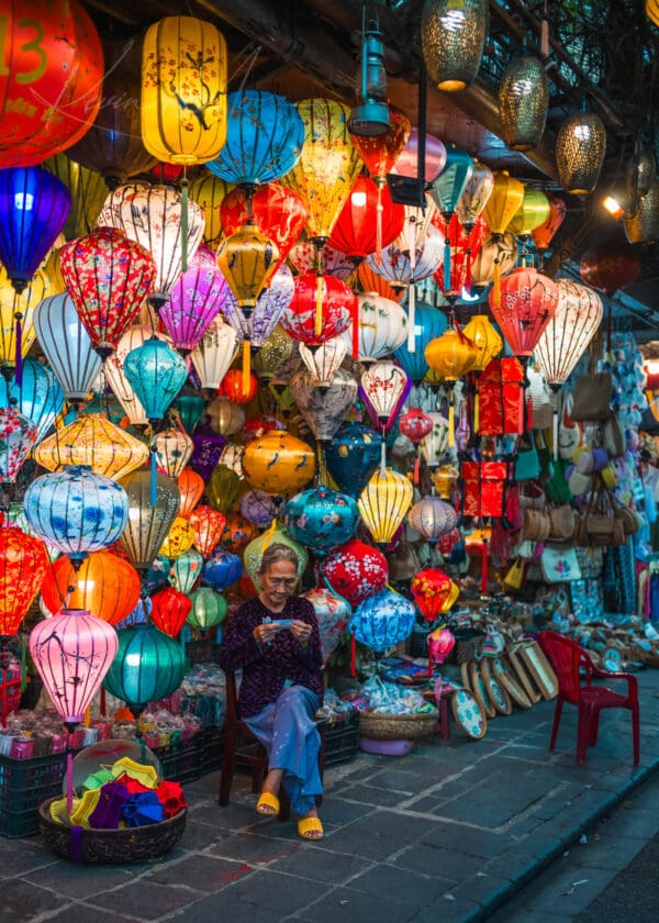 Shopkeeper amidst colorful traditional lanterns in Hoi An, Vietnam at dusk