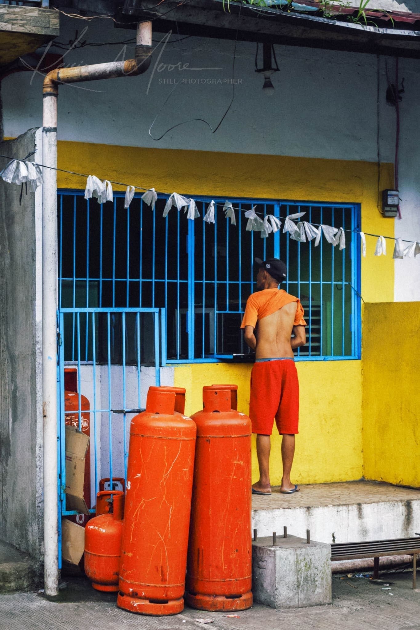 Man at window in colorful urban setting with red gas cylinders.