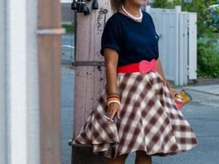 1950s-inspired street style portrait in a tranquil suburban setting, featuring plaid skirt and saddle shoes.