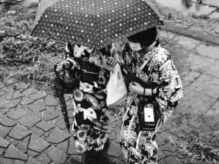 B&amp;W film photo image, taken in Iwaki City, Fukushima, Japan, captures two young women clad in traditional Japanese yukata huddled under a shared umbrella