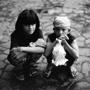 Filipino children selling Sampaguita flowers on cobblestone in moody black and white portrait