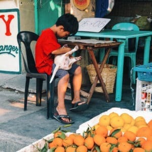 Boy engrossed in playing with puppy at vibrant street market in urban Philippines.