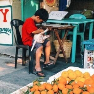 Boy and Puppy Street Photography Art Print, taken with a Fujifilm X100V, featuring a young boy cradling a puppy at a market in Pampanga, Philippines.