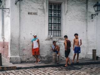 Urban street corner with young men gathering, old building backdrop, casual attire.