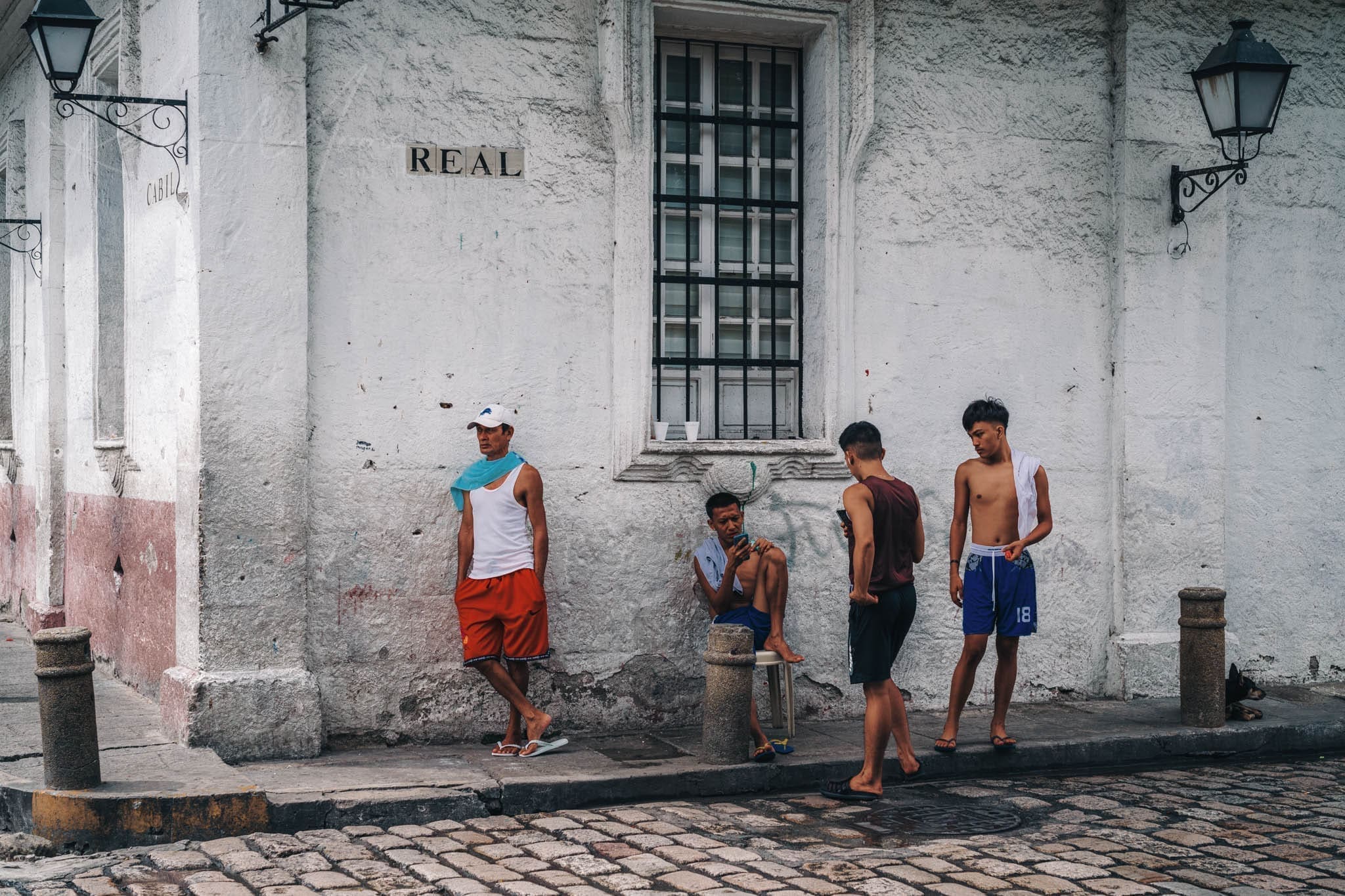 Urban street corner with young men gathering, old building backdrop, casual attire.