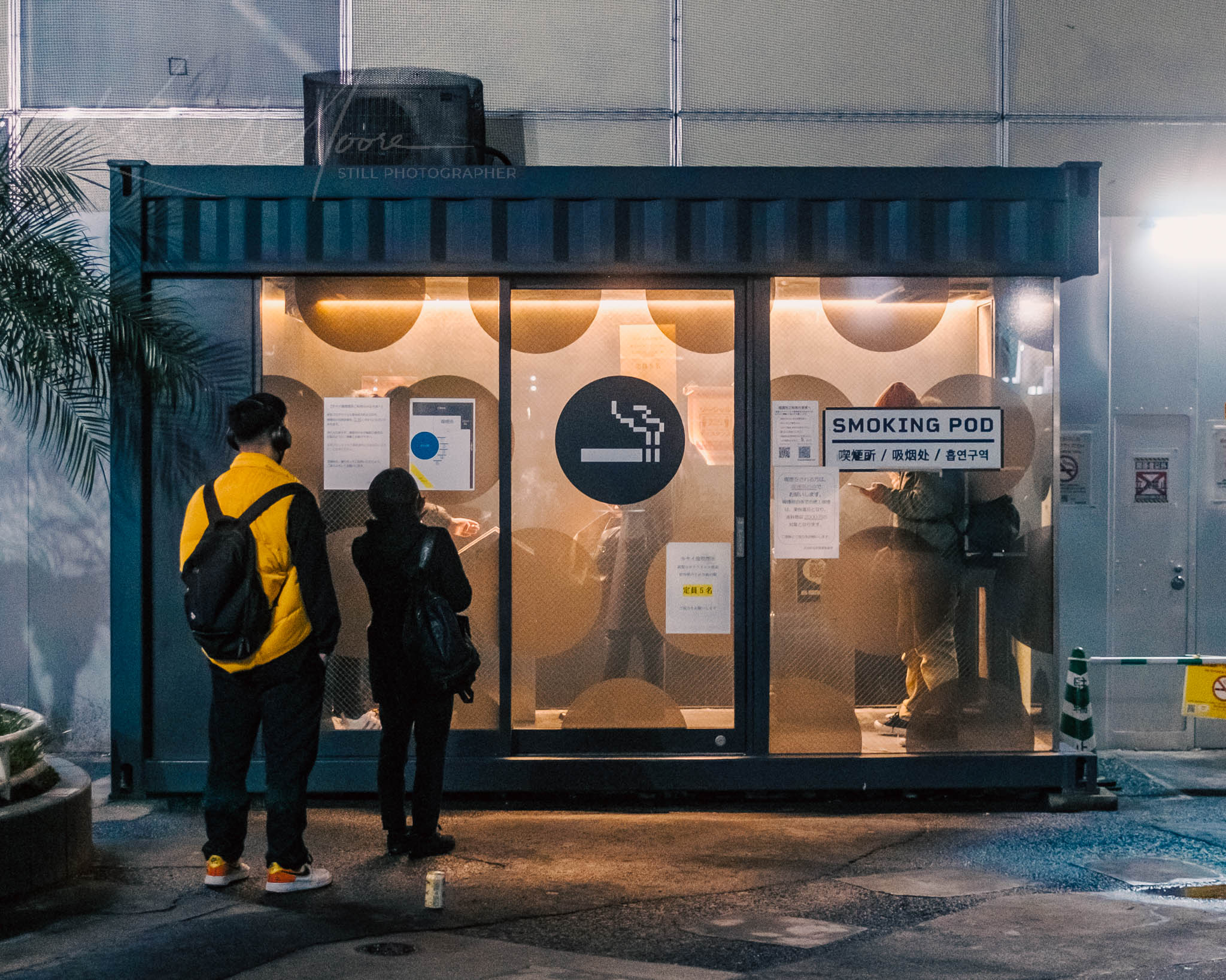 Modern Tokyo Tokyo Smoke Area at night with warm interior lighting and individuals at entrance.