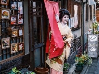 Geisha in kimono holding banner in historic Japanese alleyway