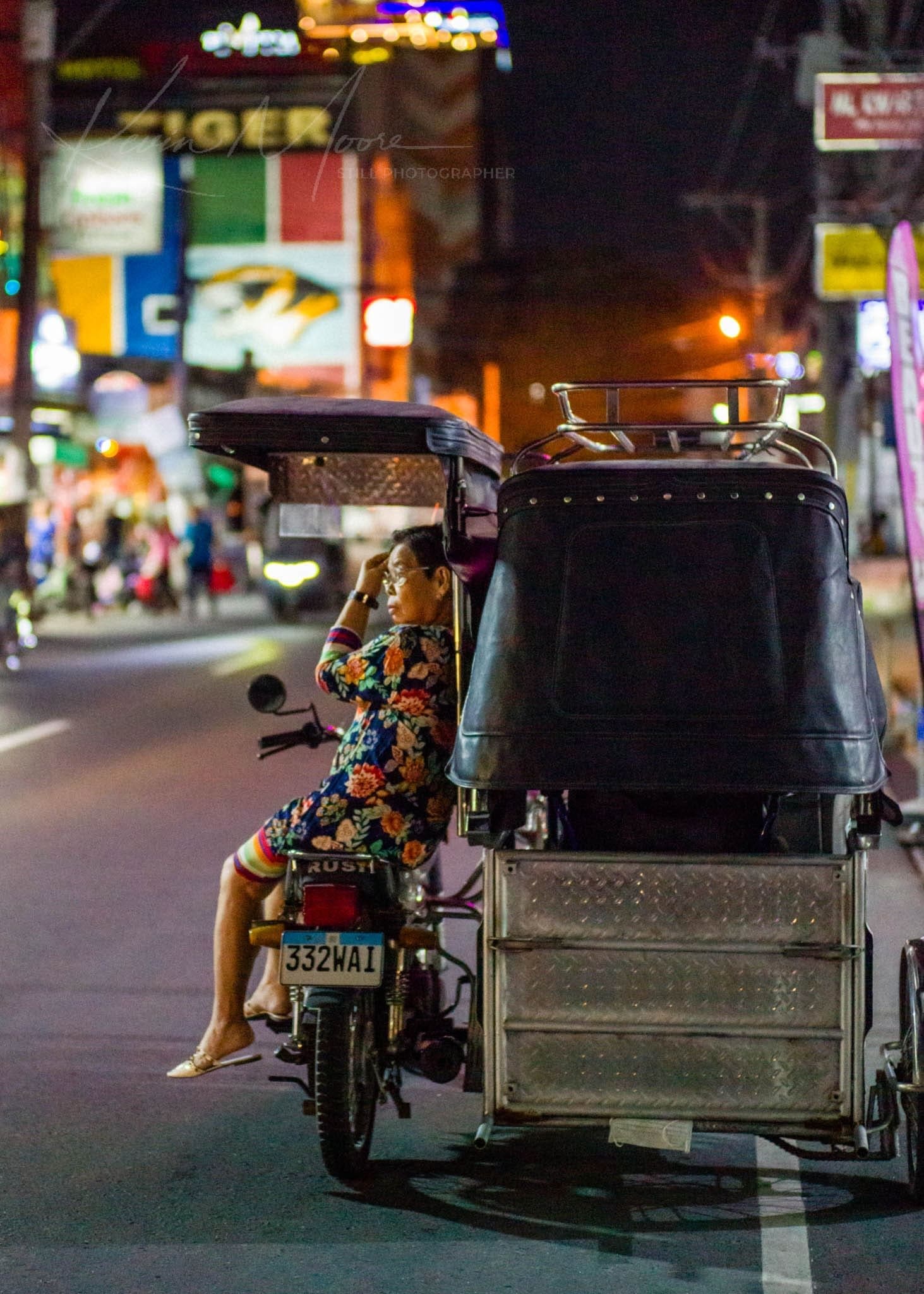 Woman on phone in tuk-tuk amidst vibrant Southeast Asian city night scene.