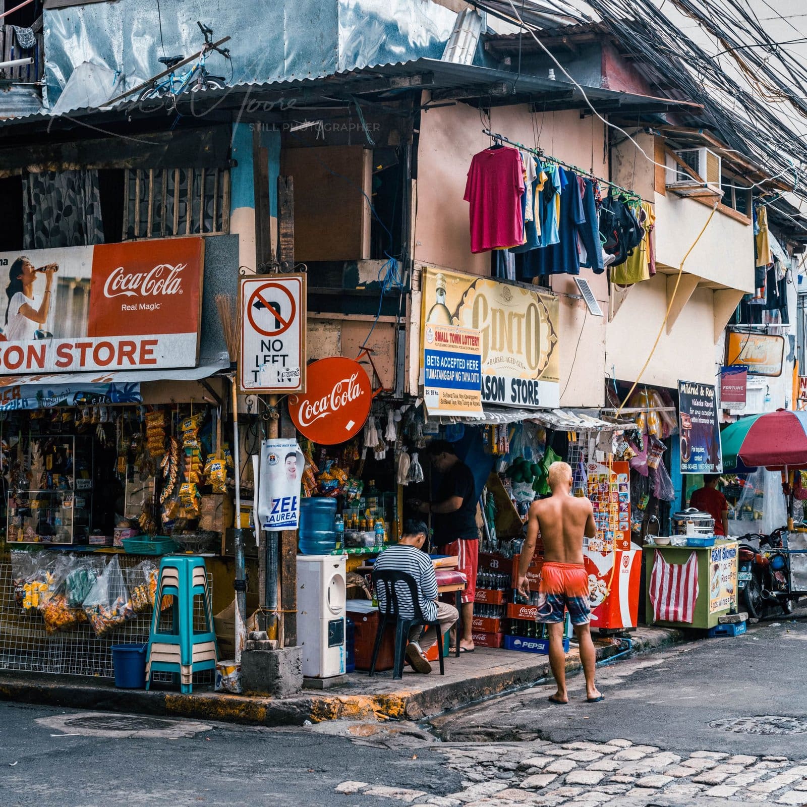 Busy urban street corner with shops, Coca-Cola signs, and lively community interactions.