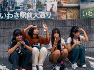Japanese girls Enjoying a Tech-Savvy Break in Urban Japan Japanese girls enjoying a leisurely break on a city curb in Japan.