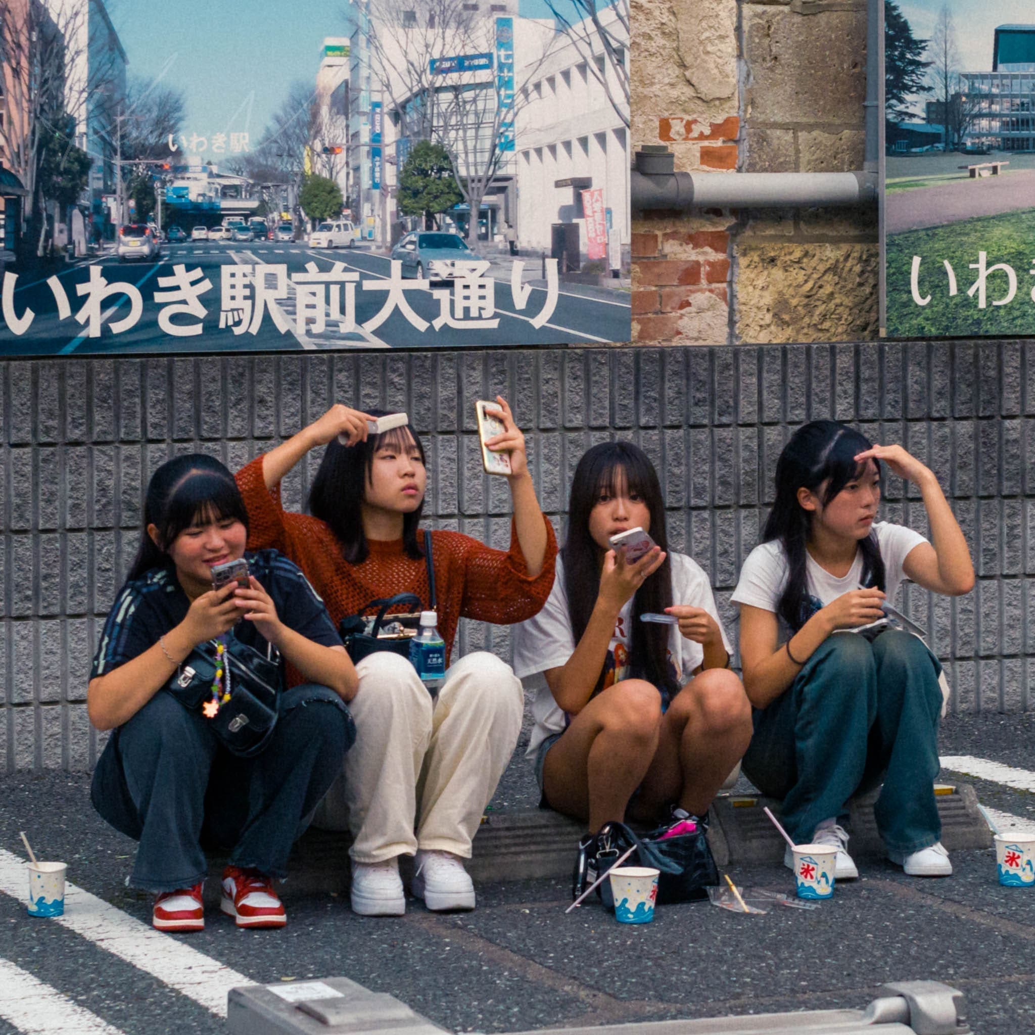 Four young women enjoying a leisurely break on a city curb in Japan.