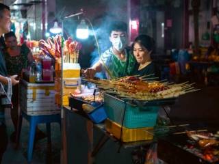 Bustling Hanoi night market food stall with skewered treats and attentive vendors.