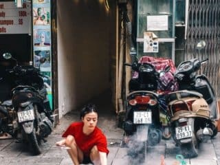 Burning Ritual Amidst Hanoi Urban Bustle Vietnamese woman performing street ritual with fire amidst urban setting with motorbikes.