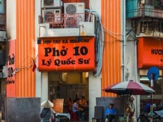Street vendor and diners at Phở 10 L&yacute; Quốc Sư restaurant in a vibrant Vietnamese city.