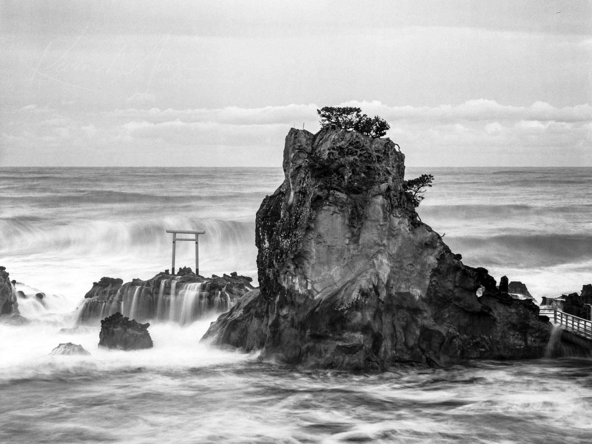 Dramatic cliff and Shinto torii gate on rugged Japanese coastline.