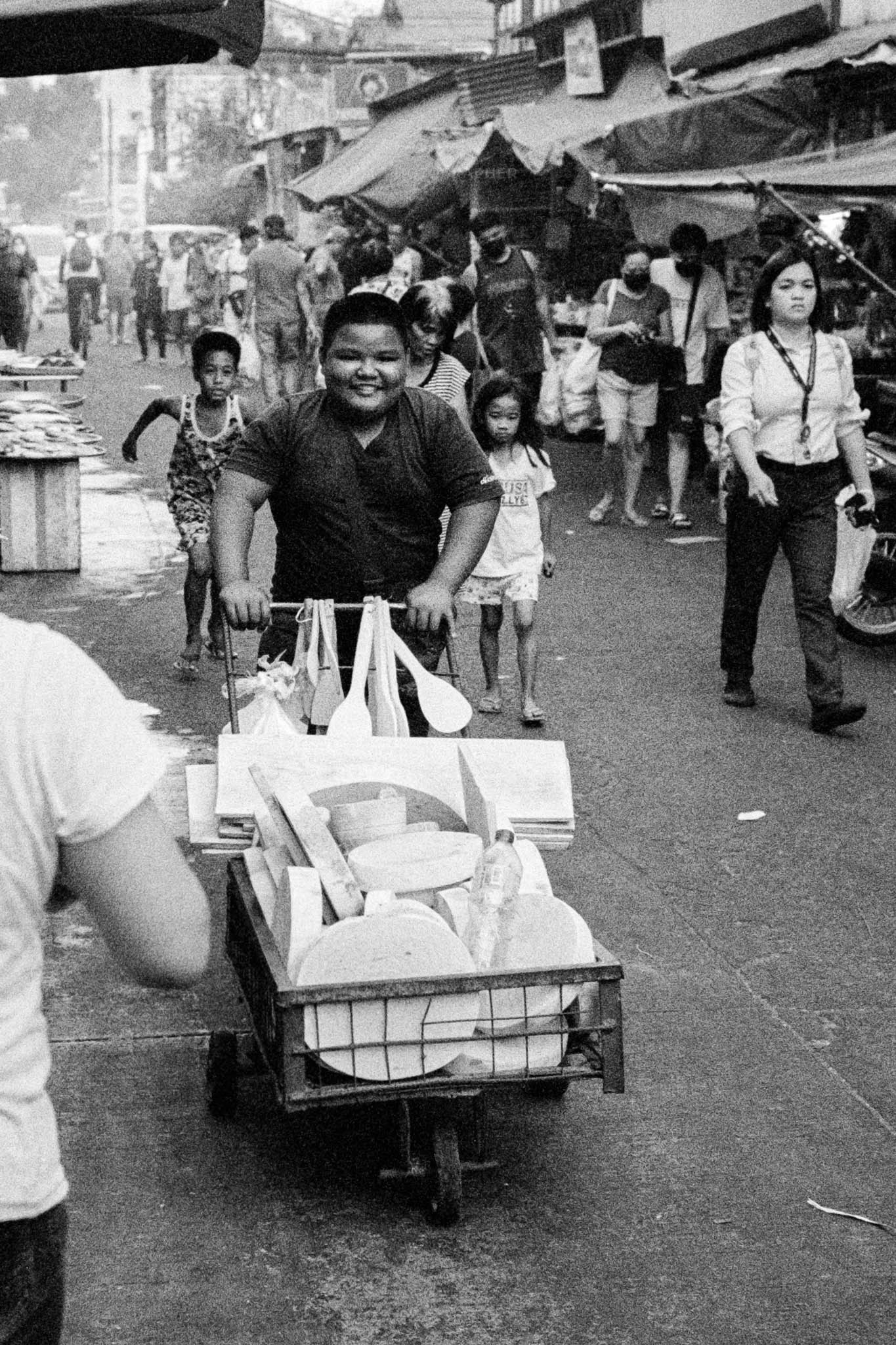 Young man pushing cart at vibrant street market in grayscale.