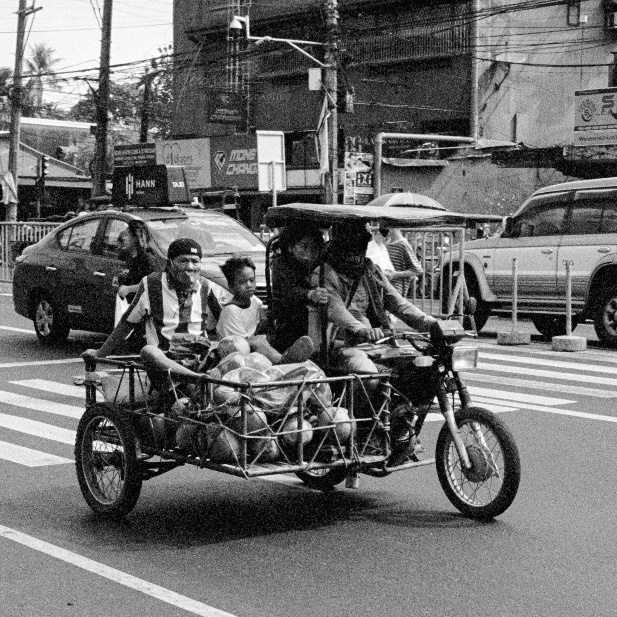 Busy city street with family riding a packed motorcycle tricycle.