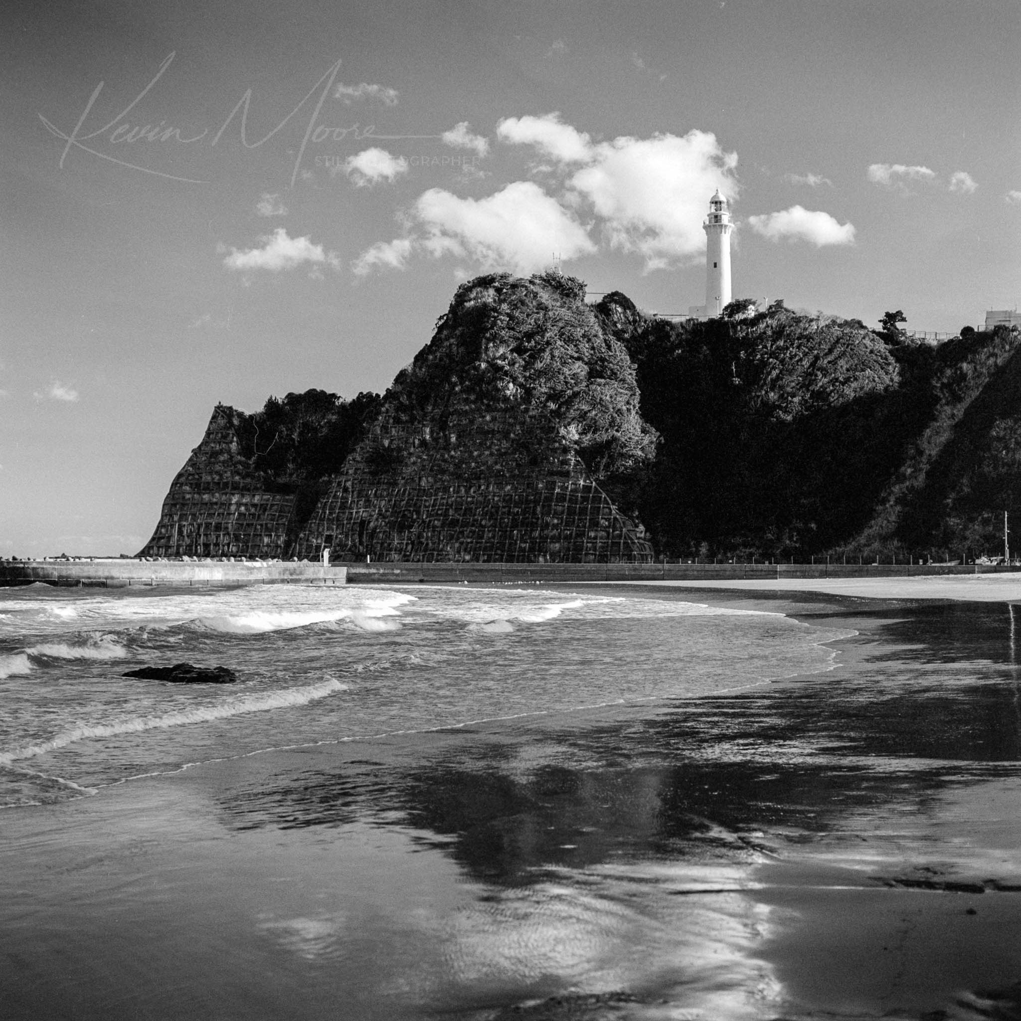 Lighthouse on a rocky coastal headland with safety mesh and ocean waves.