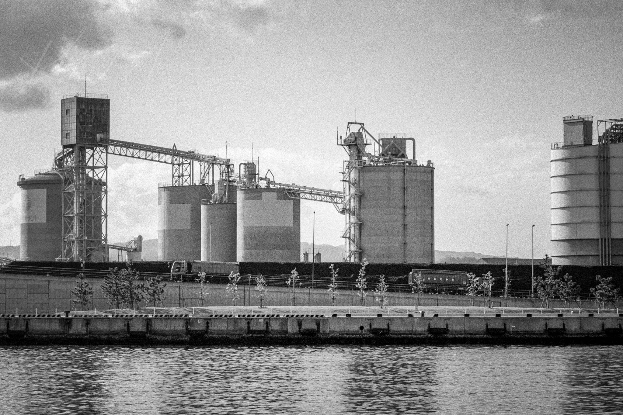 Riverside Factory with Industrial Silos and Docked Freight Train in Black and White