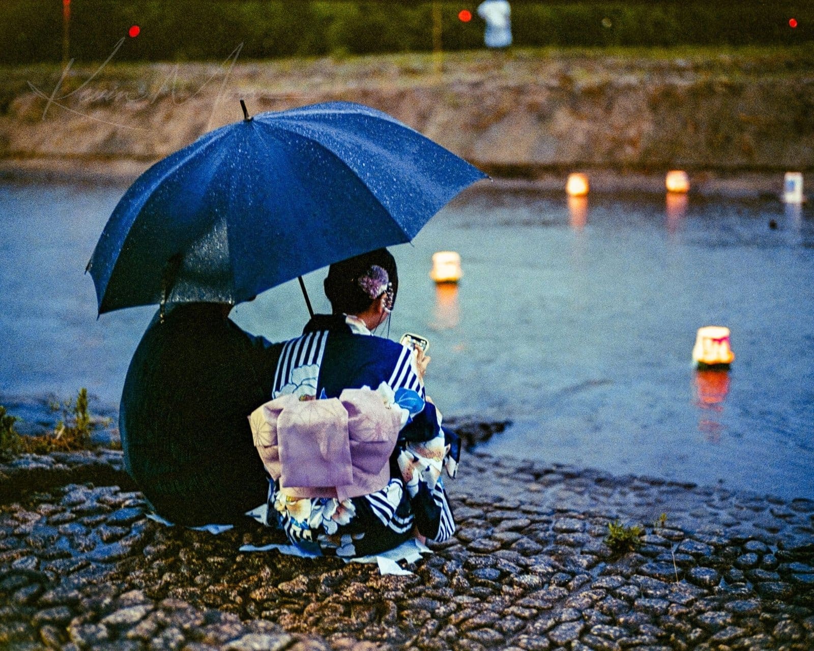 Japanese Lantern Festival A couple in traditional Japanese attire sitting by a river with floating lanterns at twilight.