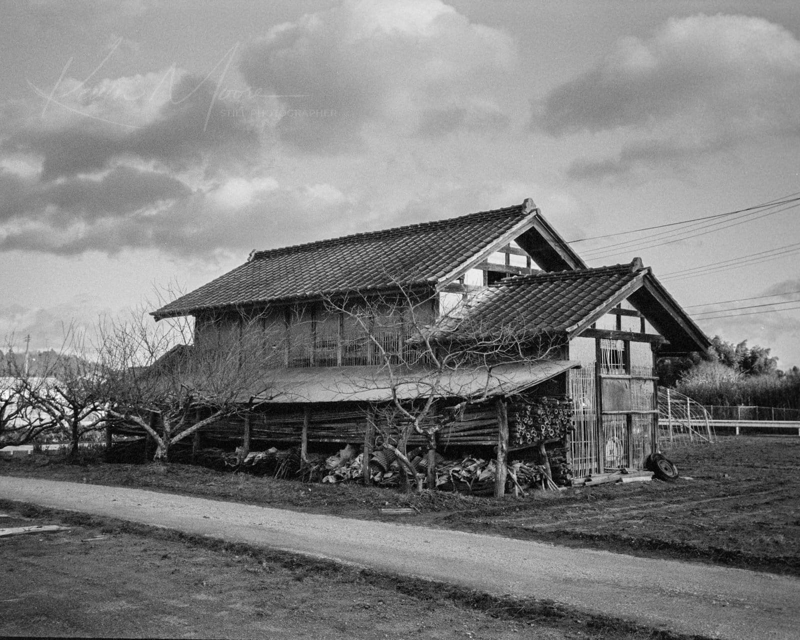 Weathered Japanese barn raised on posts under a dramatic winter sky, bare trees in front, rural Iwaki, Fukushima