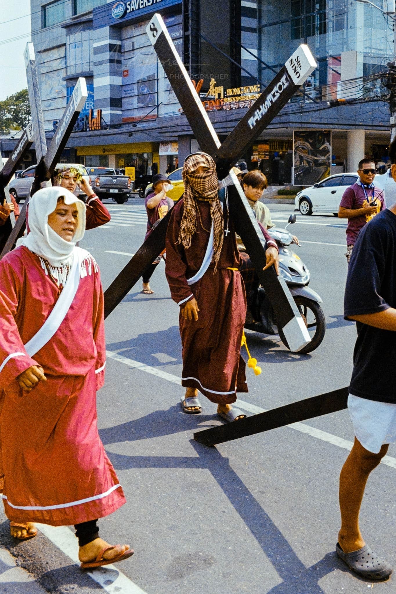 Religious procession in city street with participants carrying crosses.