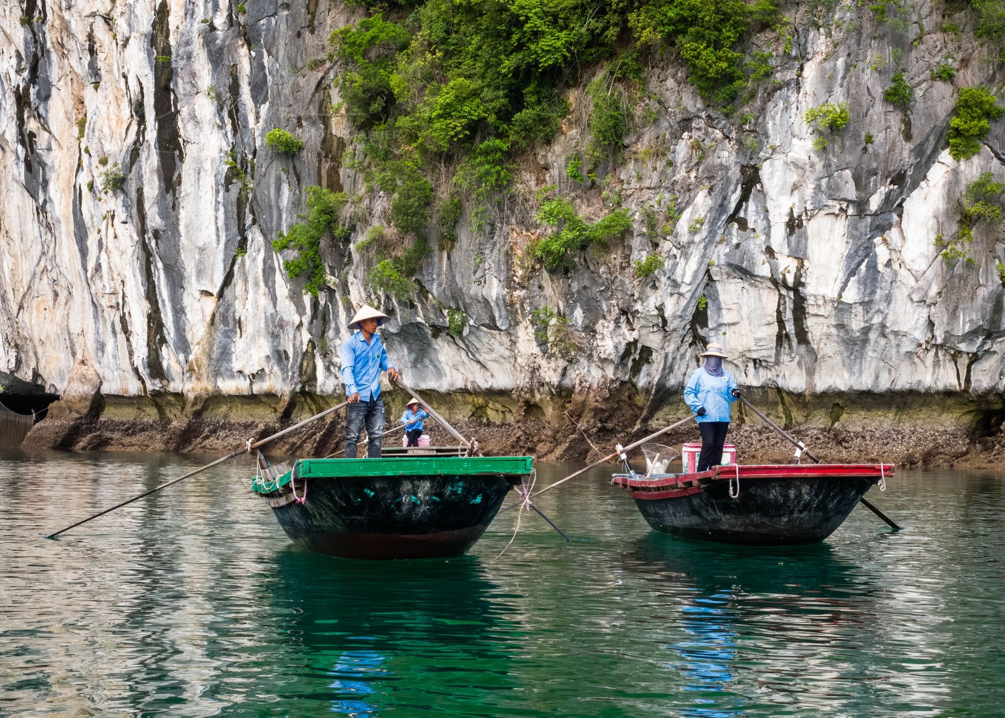 Traditional Asian rowboats navigating calm emerald waters near limestone karst cliffs Ha Long Bay.