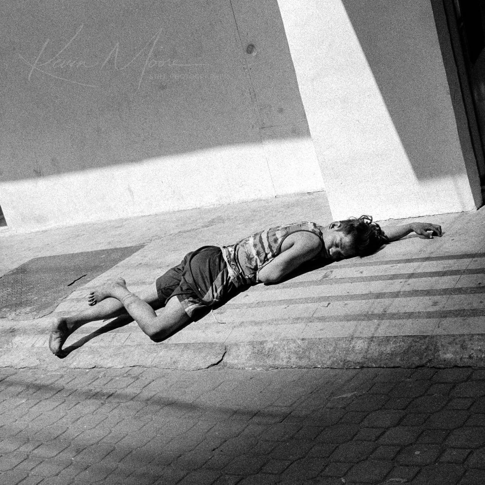 Young Rugby addict boy resting on sidewalk in harsh sunlight captured in monochrome.