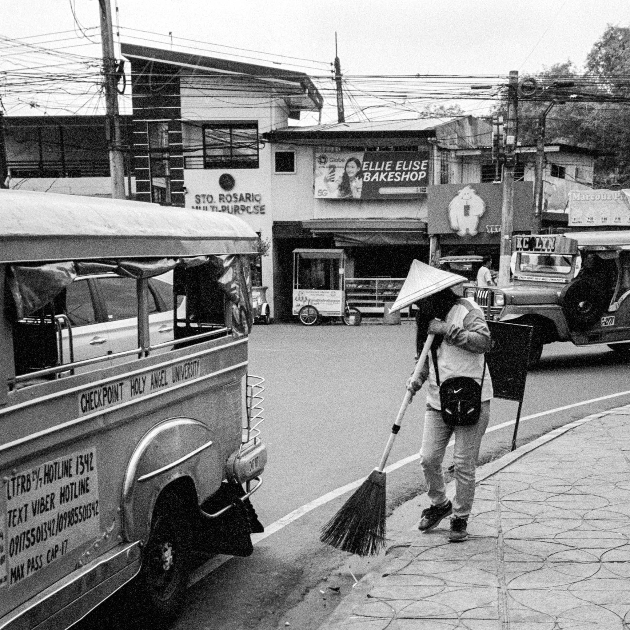 Street sweeper with conical hat near decorated jeepneyn the Philippines.