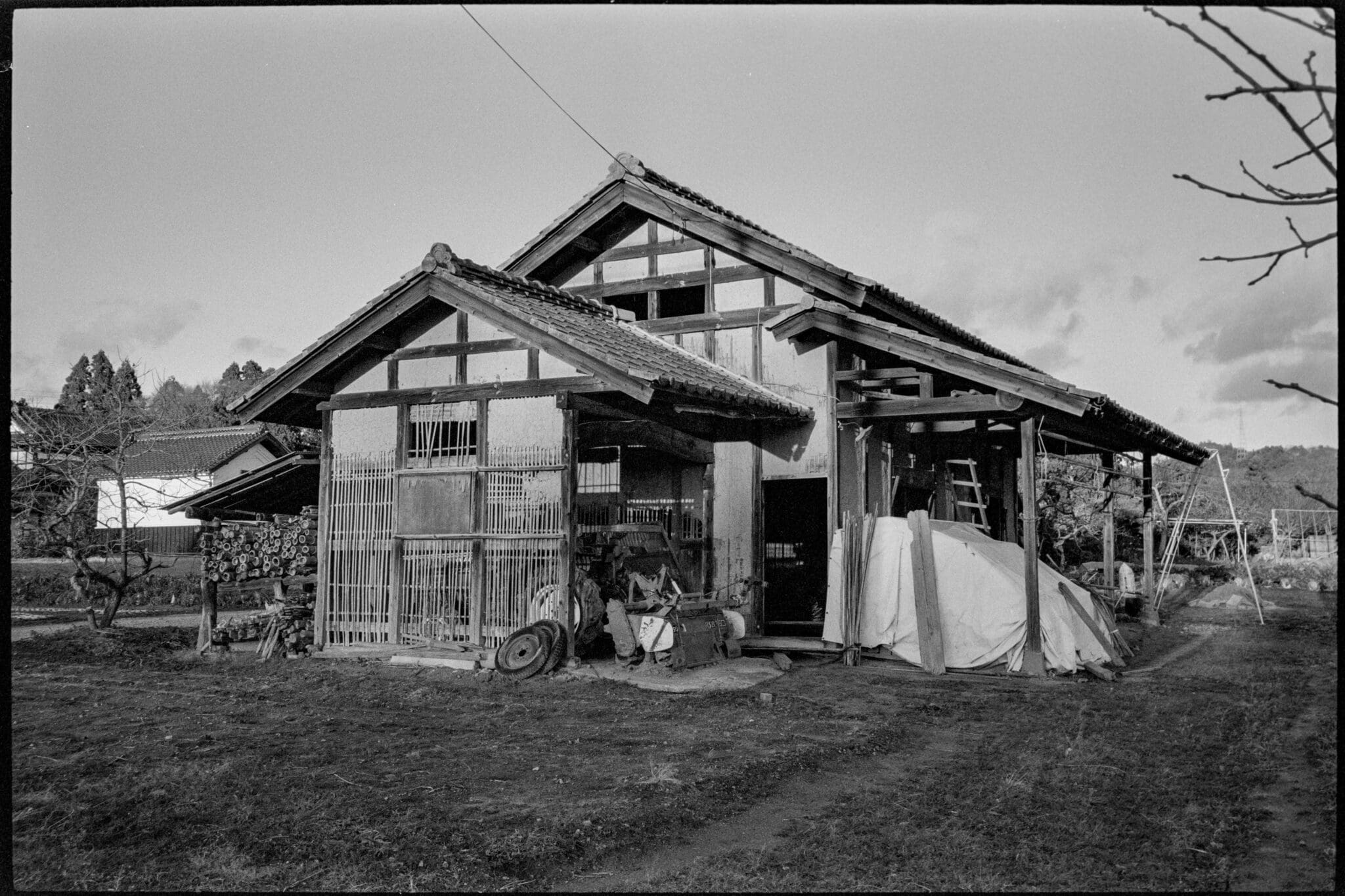 Black and white photo of an old, traditional rural house with scattered farming equipment.