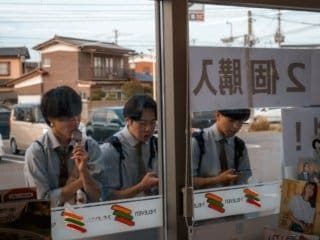 Japanese students in uniforms engage with ice cream and smartphones by a window.