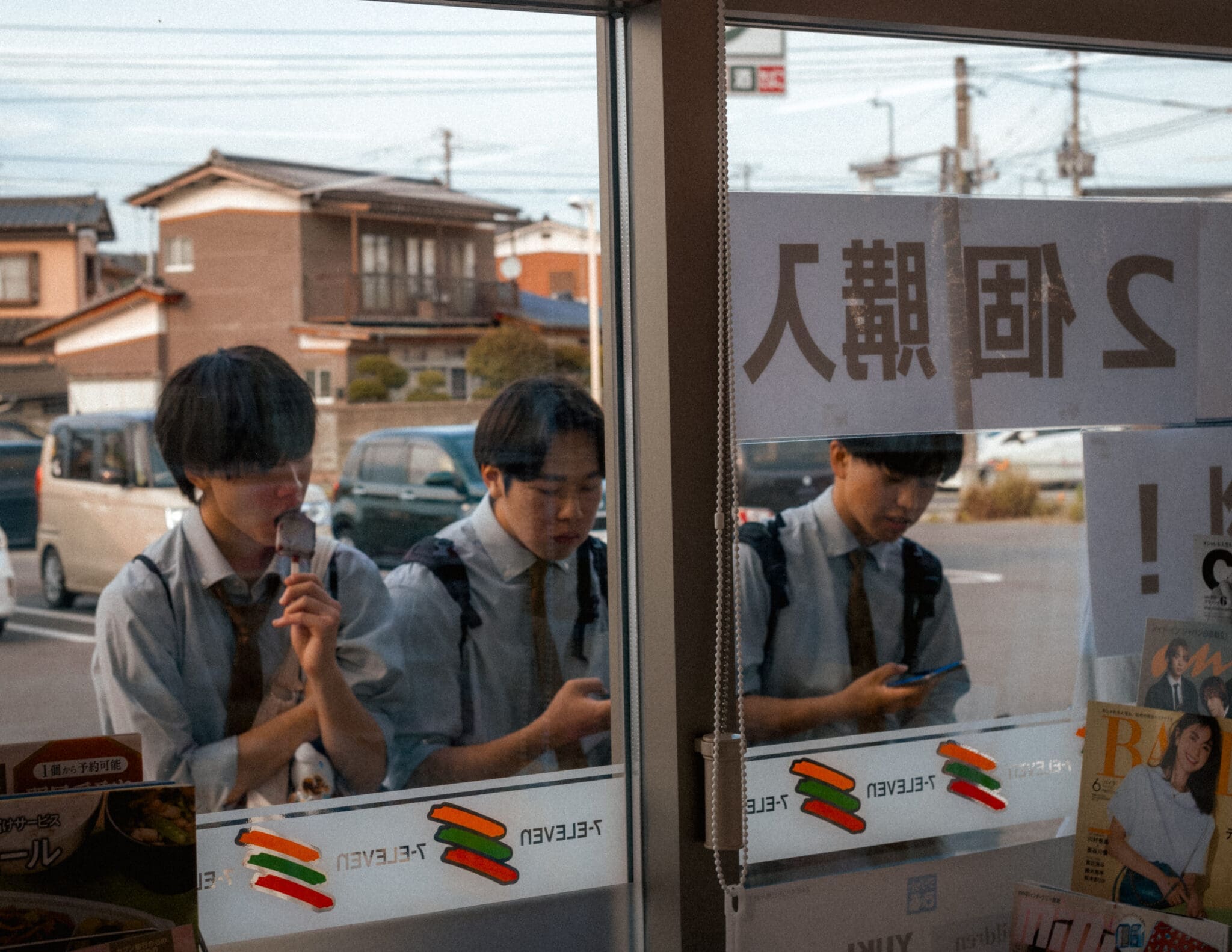 Japanese students in uniforms engage with ice cream and smartphones by a window.