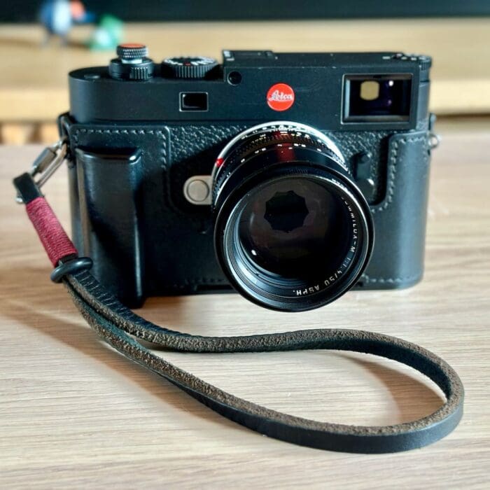 Leica M11 rangefinder camera with Summilux 50mm f/1.4 ASPH lens and strap on wooden table.