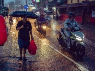 Rain-soaked Philippines city street with pedestrians and motorcyclists at dusk.