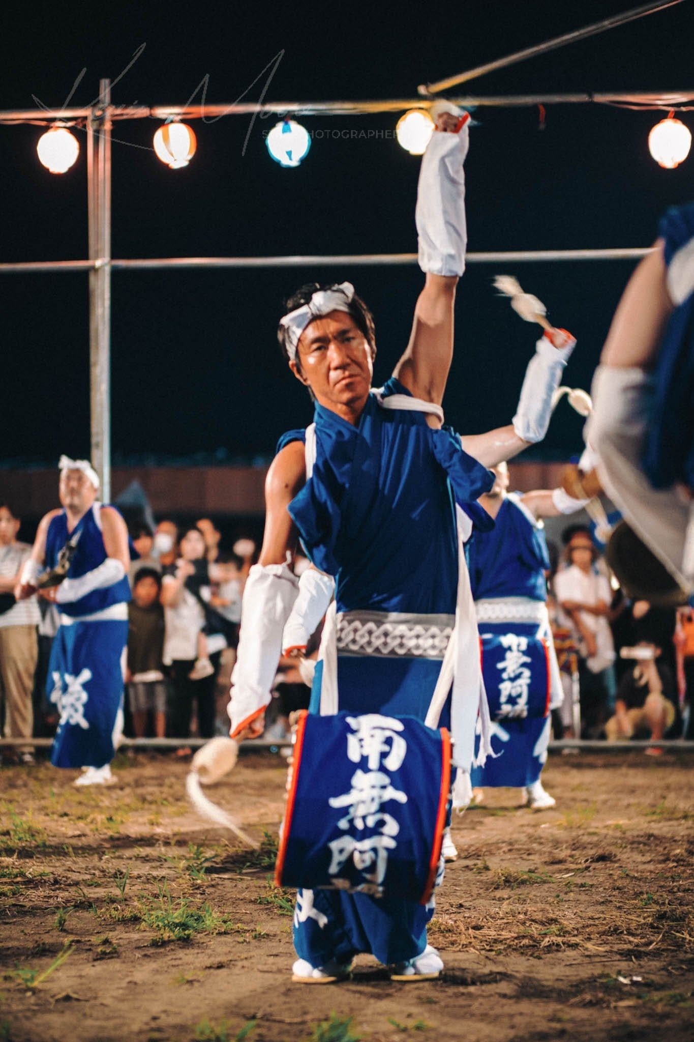 Traditional Japanese festival dance performance under string lights at night.