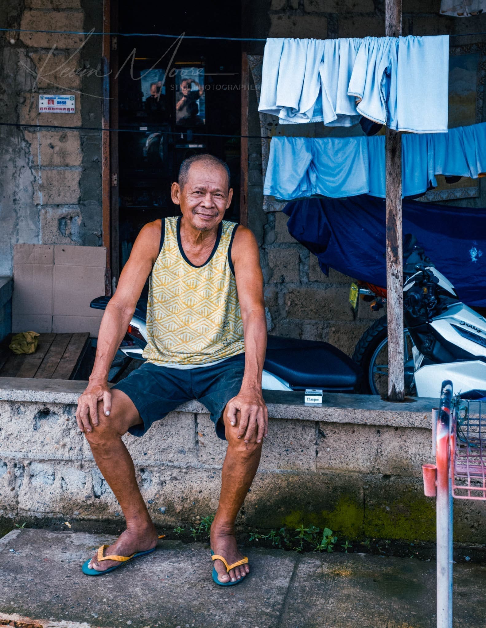 Senior man relaxes outdoors, surrounded by laundry and a motorbike.