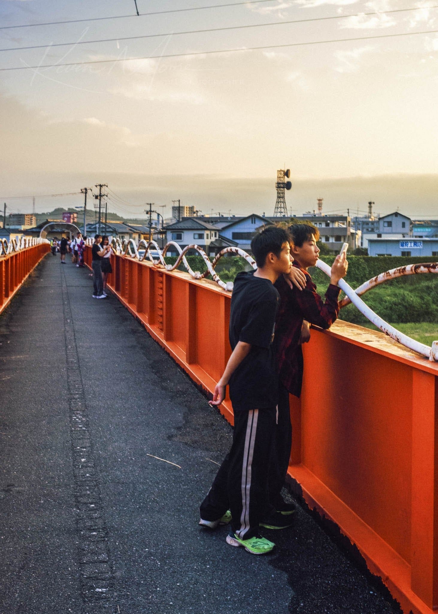 Sunset on an orange pedestrian bridge with people walking and chatting.