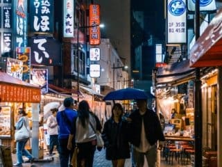 Busy Tokyo street at night with neon signs and people under a blue umbrella.