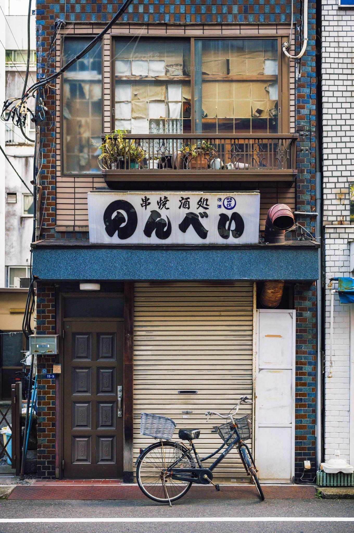 Narrow urban building in Japan with bicycle and potted balcony plants.